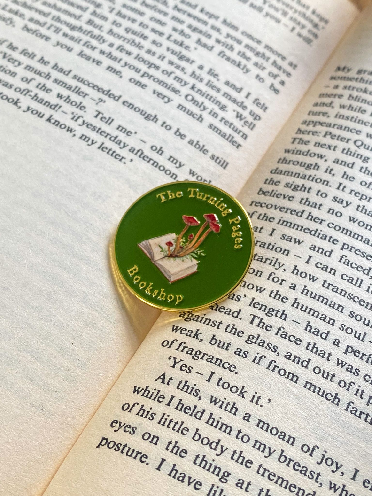 The Turning Pages Enamel pin sits on an open book